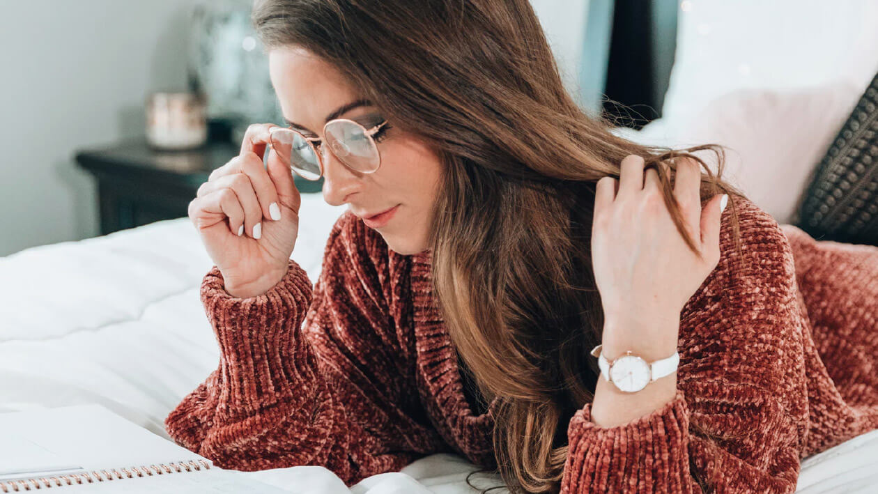 A girl holding her spectacles and lying on the bed