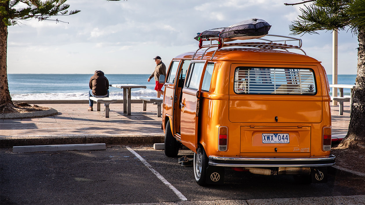 An orange color car parked near a street with two persons