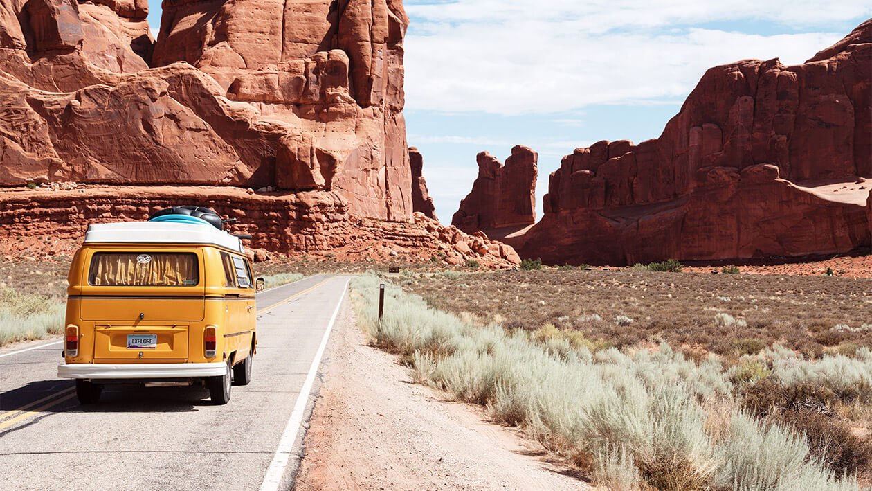 An orange car running on a lonely street of valley