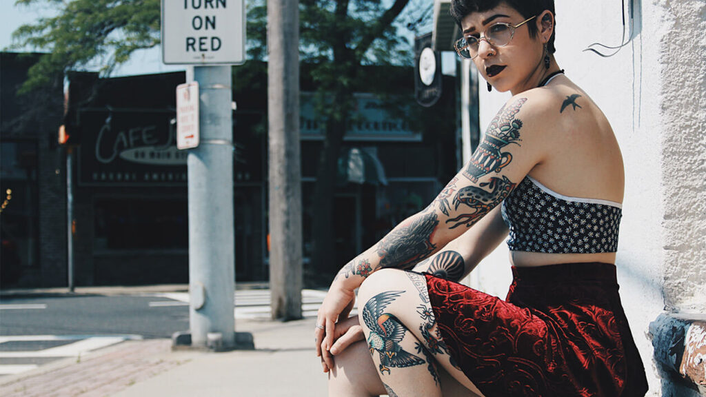 Tattooed woman sitting on sidewalk edge.